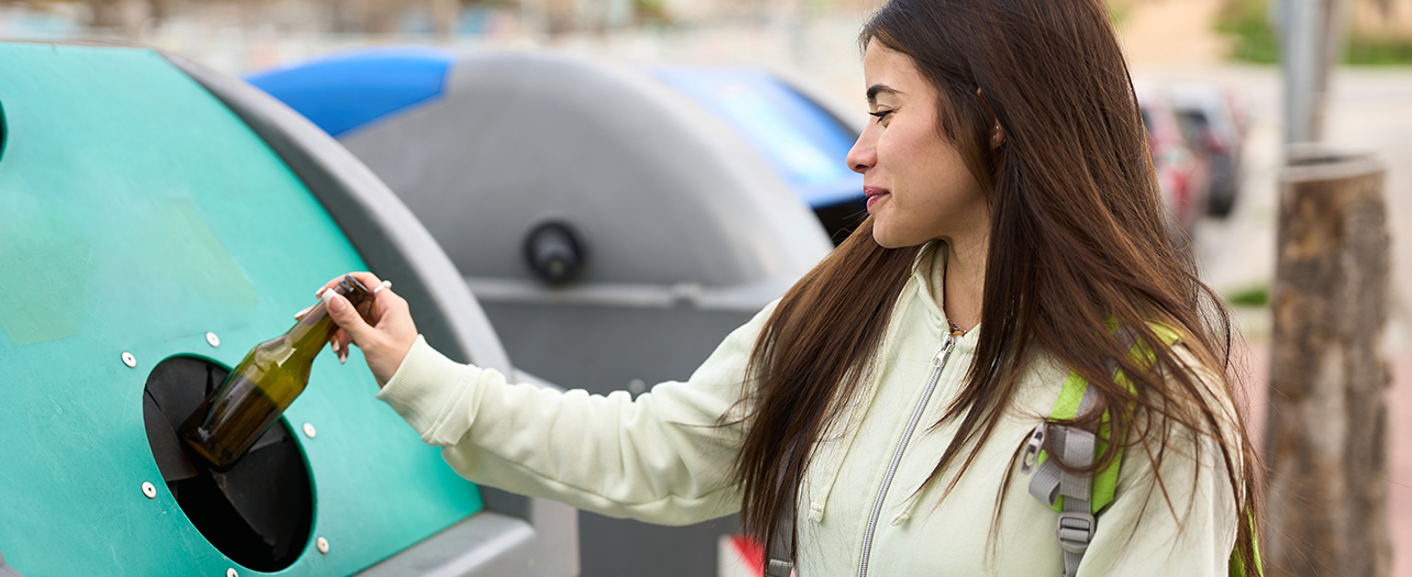 woman recycling a glass bottle in an outdoor recycling bin