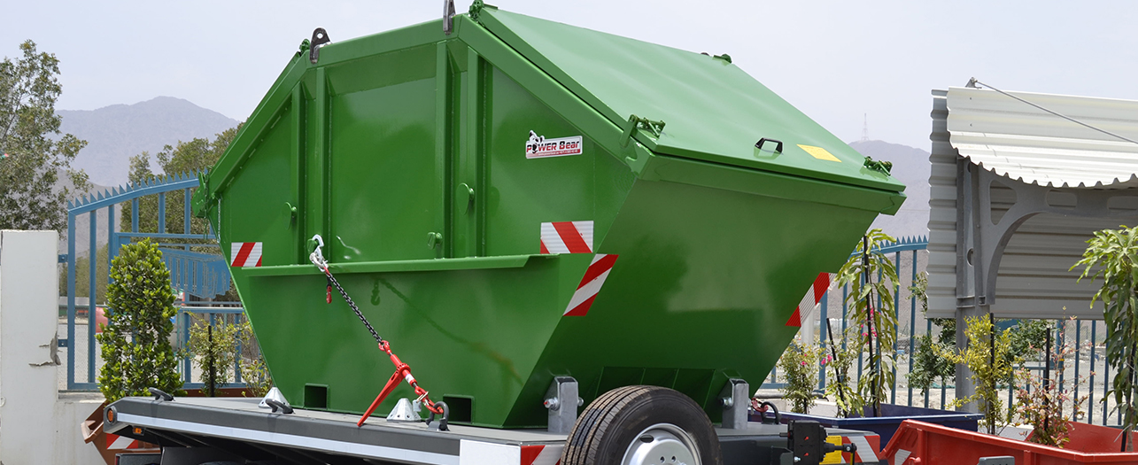 Green metal skip container mounted on a dual-axle trailer.
