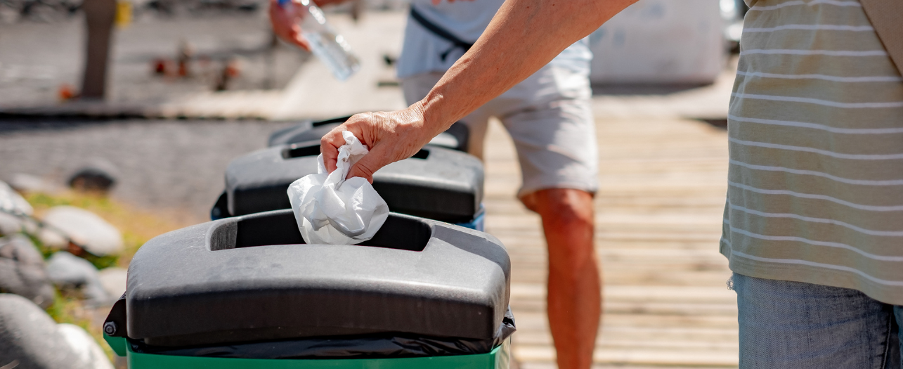 People throwing trash into a beachside bin