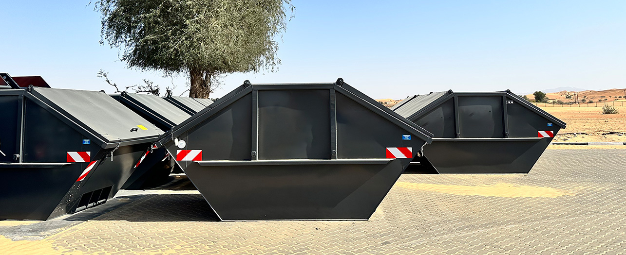 Black waste skip containers lined up in a desert area