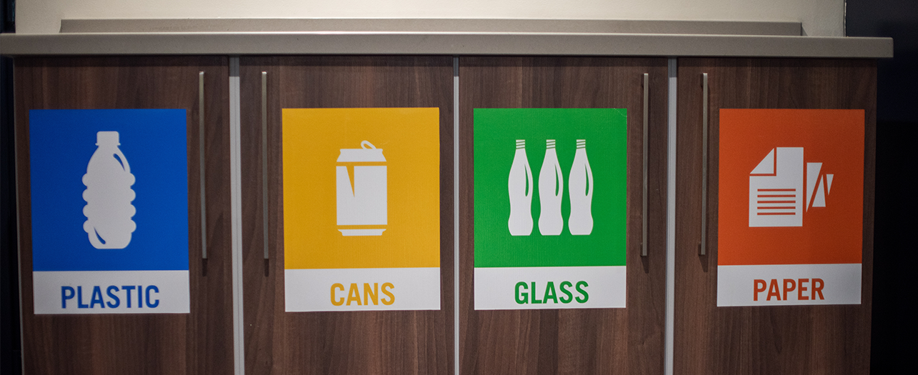 Indoor recycling bins labeled for plastic, cans, glass, and paper